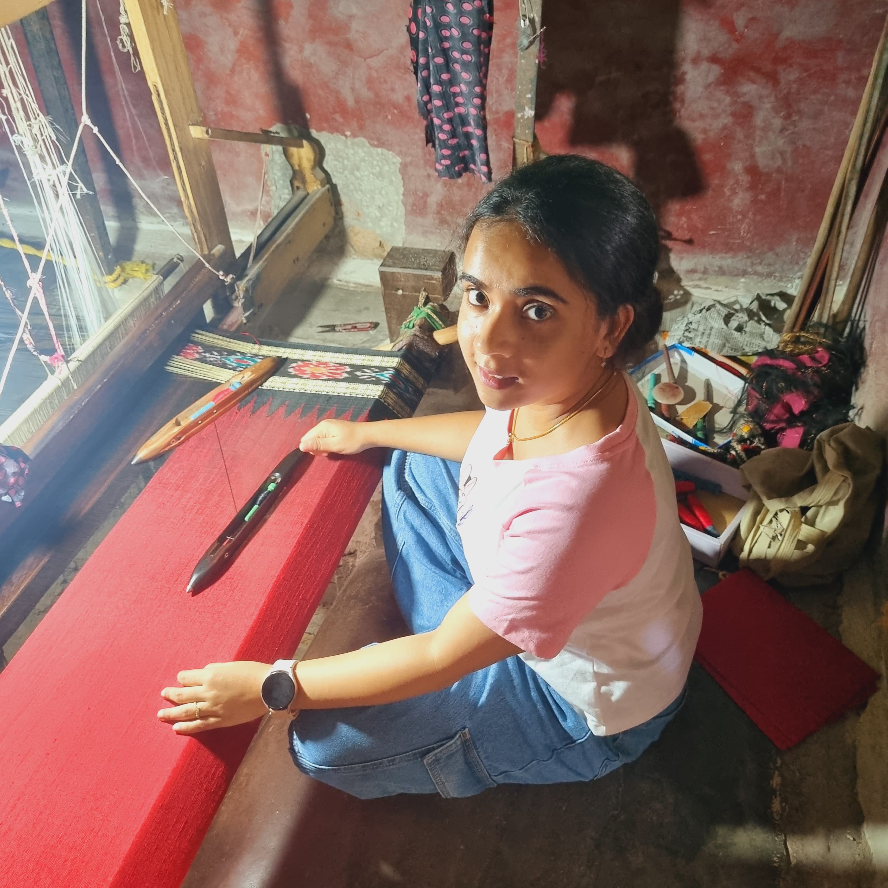 Young woman weaving bright red fabric on a floor handloom
