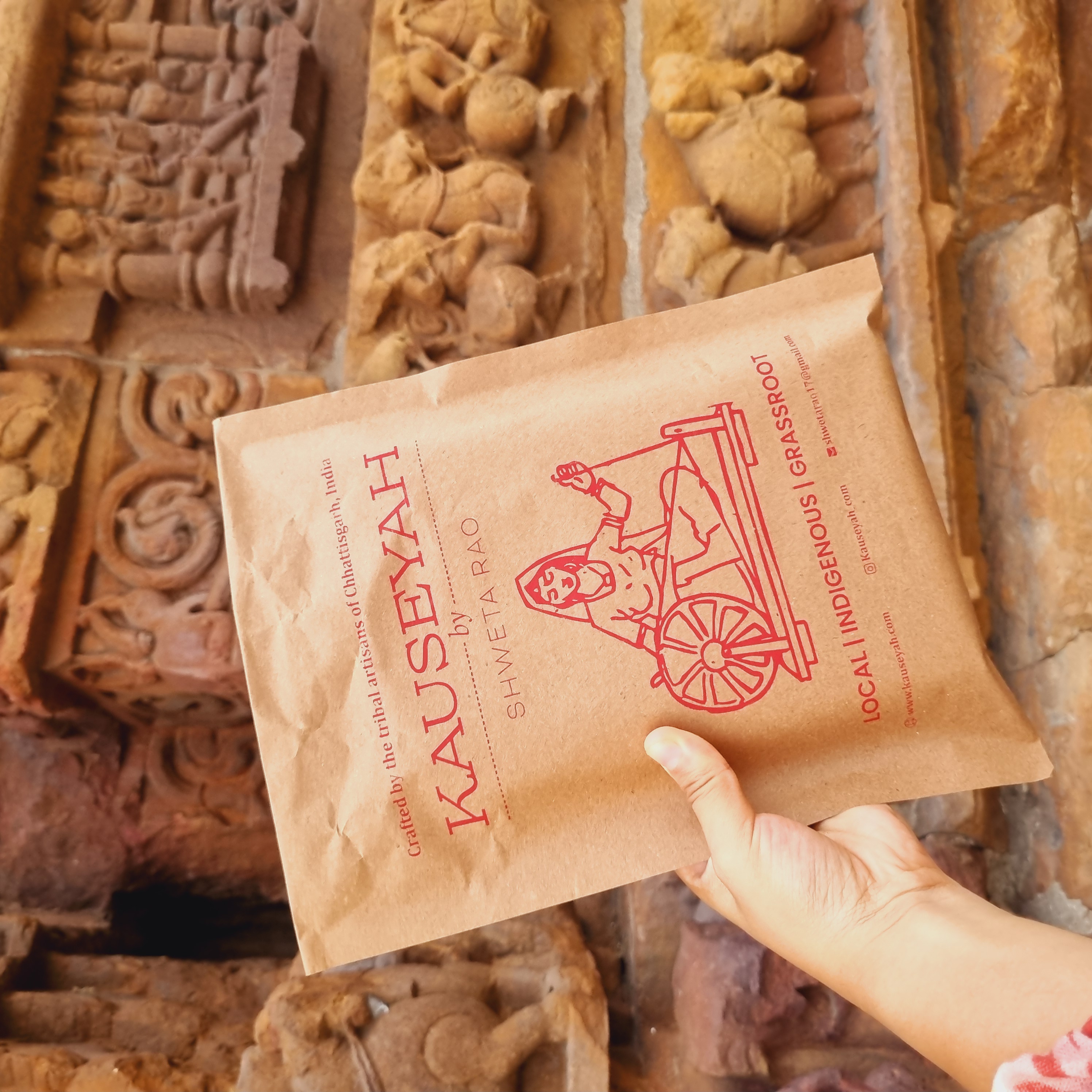 Kauseyah branded kraft envelope against ancient stone temple carvings