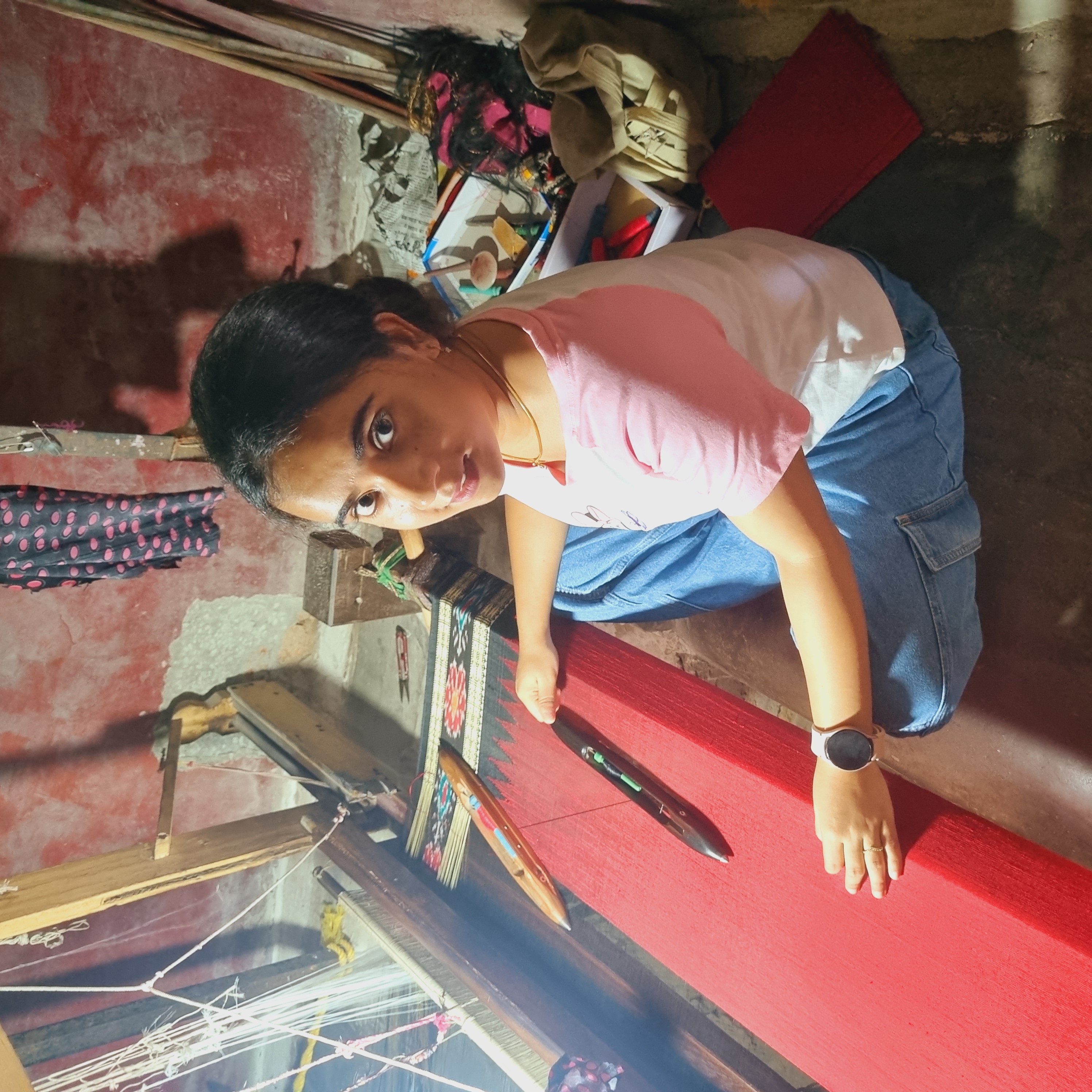 Young woman weaving bright red fabric on a floor handloom