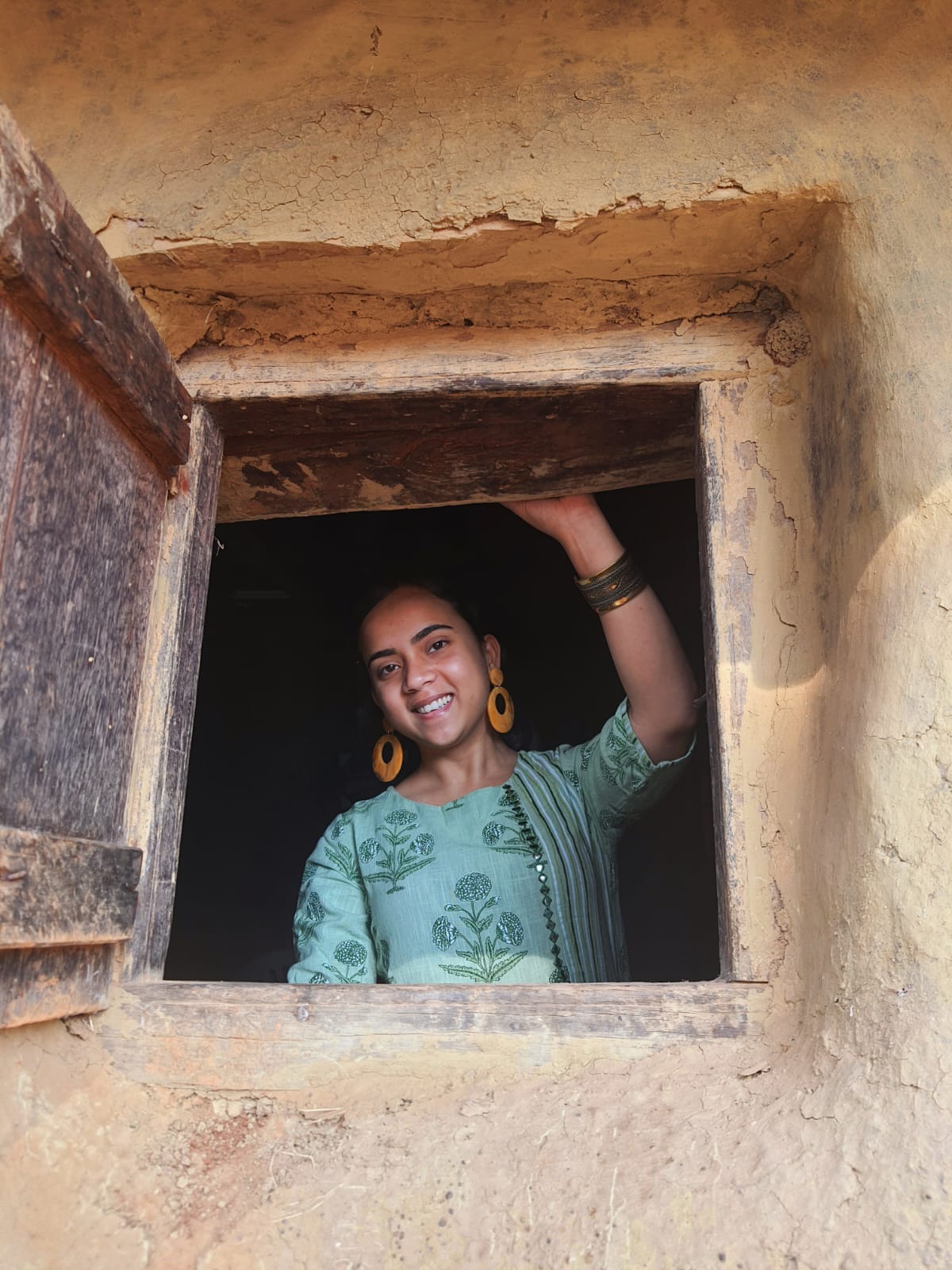 Woman in mint green block-print kurta at a rustic mud-house window